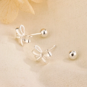 Close-up of matte silver bow stud earrings with secure screw-back on linen fabric