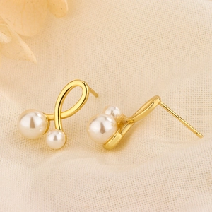 Macro shot of gold cross pearl earrings with S925 silver needles on beige fabric background