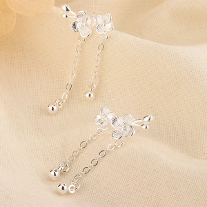 Detailed view of silver flower tassel earrings with plum blossom design on beige fabric