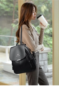 Modern black leather backpack for women shown in use by a model near a bright window