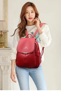 Close-up of deep red leather backpack showing textured flip-top lid and metal logo buckle