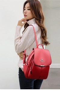 Detail of red pebbled leather backpack showing silver kangaroo logo and side zip pocket