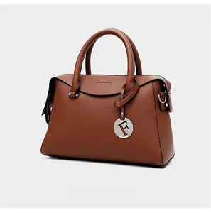 Détail de sac à main marron caramel en cuir grainé avec pendentif lettre F argenté