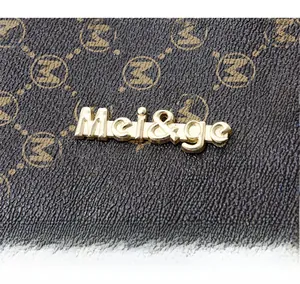 Gros plan sur cuir synthétique marron texturé avec motif M et logo en métal doré brillant