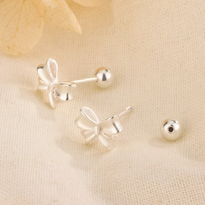 Elegant silver bow stud earrings with secure screw-back ball design on soft fabric