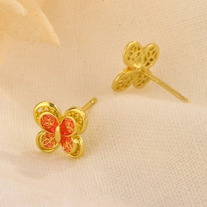 Macro detail of gold butterfly stud earrings featuring orange enamel and filigree textures