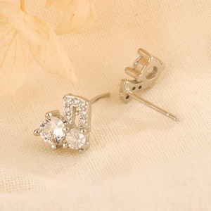 Macro detail of silver musical note earrings with sparkling zircon on linen texture