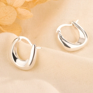 Macro detail of silver minimalist U-shaped hoop earrings on beige linen fabric texture