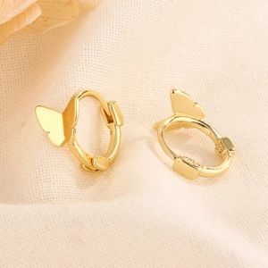 Minimalist gold butterfly huggie hoop earrings displayed on textured beige linen
