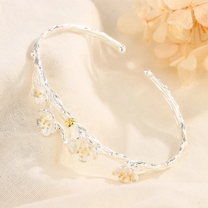 Detailed close-up of silver branch bangle with golden plum blossoms on textured fabric