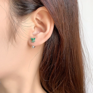 Elegant silver butterfly stud earrings with emerald green zircon stones on model ear