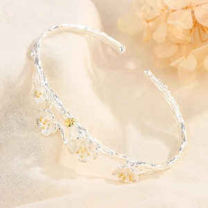 Floral branch cuff bracelet in silver and gold tones on a textured linen background