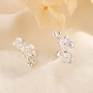Macro detail of plum blossom silver stud earrings with matte texture on beige fabric