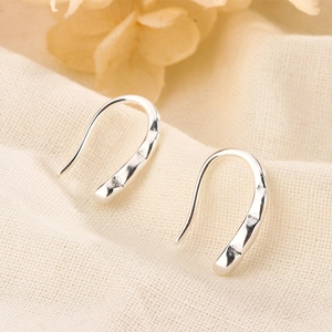 Detail of silver U-shaped hook earrings with hammered texture on natural linen background