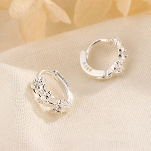 Macro detail of silver flower earrings showing S925 hallmark and sparkling zircon petals