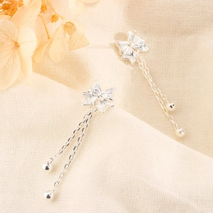 Macro detail of silver bow earrings with filigree craftsmanship and long tassel fringe