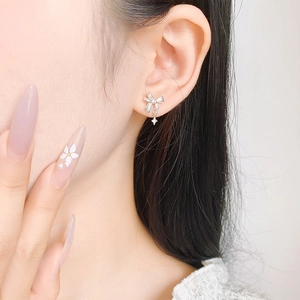 Detail of silver bow tassel and star stud earring worn on a model's earlobe