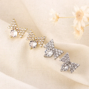 Close-up of gold and silver bow stud earrings with sparkling pavé cubic zirconia on fabric