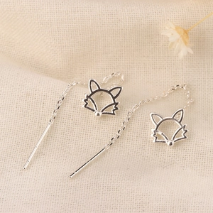 Minimalist silver hollow fox tassel earrings on a textured linen background with a dried flower