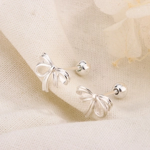 Detail of silver ribbon bow earrings with secure screw back on linen fabric