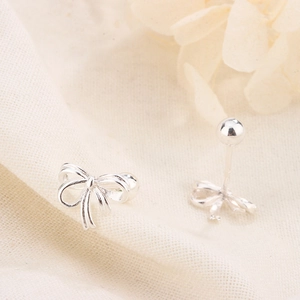 Macro detail of polished bow-shaped stud earrings on minimalist cream fabric