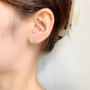 Elegant gold bow earrings with a central sparkling crystal on a model ear