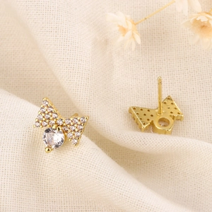 Exquisite gold bow stud earrings with clear zircon crystals on white fabric background