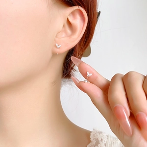 Macro shot of silver butterfly stud earring with sparkling zircon on earlobe