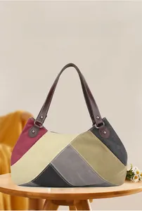 Detail of color-block canvas tote bag with brown leather handles on a wooden stool