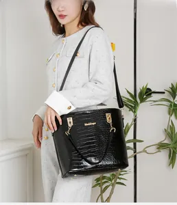 Détail d'un sac cabas noir motif crocodile avec ferrures dorées et bandoulière amovible