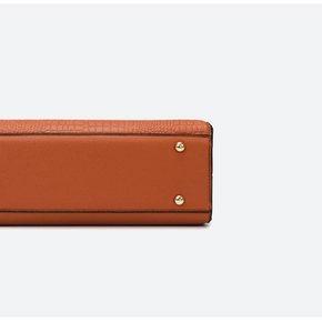 Detail of orange tote bag bottom with lychee and crocodile leather patterns and gold studs
