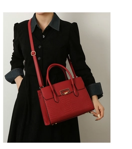 Detail of red crocodile embossed handbag with gold metal clasp and double handles