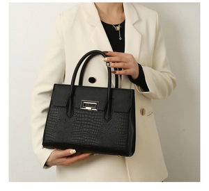 Close-up of black crocodile pattern tote bag with silver lock held by a model
