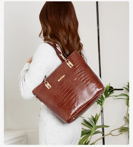 Détail d'un cabas marron à motif crocodile avec logo doré et bandoulière chaîne