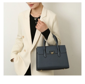 Close-up of deep blue crocodile embossed leather handbag with metal buckle and top handles