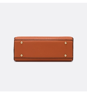 Detail view of the orange-brown bag bottom with gold studs and embossed leather texture