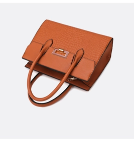 Macro view of textured crocodile pattern and rectangular metal buckle on burnt orange tote
