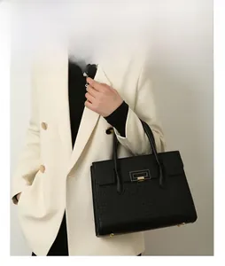 Detail of black crocodile embossed tote bag with gold metal buckle and dual top handles