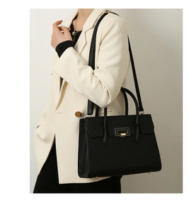 Close-up of black crocodile pattern tote bag with gold square metal lock on white suit