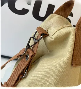 Close-up of beige canvas tote with brown thick strap and dark gray metal hook detail