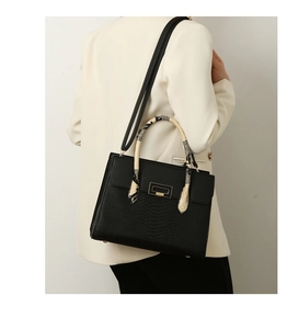 Detail of black tote bag with snakeskin embossed texture and patterned top handle