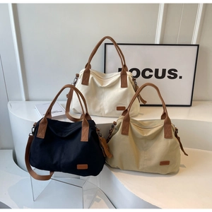 Three canvas tote bags in white black and khaki with leather trim on minimalist display