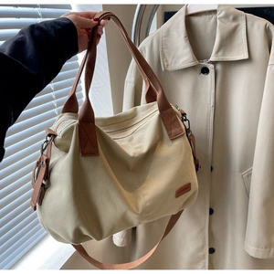 Close-up of beige canvas tote bag with brown webbing handles and leather brand patch