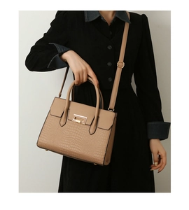 Khaki tote bag with crocodile texture and gold lock shown on model with black outfit