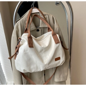 Detail of minimalist cream tote bag with brown straps and leather logo hanging on coat rack