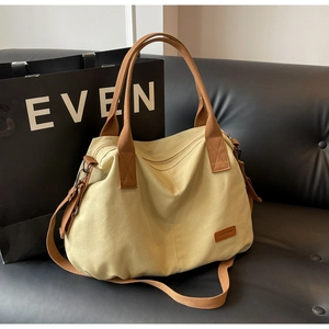 Close-up of beige canvas tote bag with brown straps on leather sofa in indoor setting