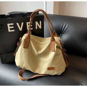 Detail of beige canvas tote bag with brown straps and brand patch on a leather sofa
