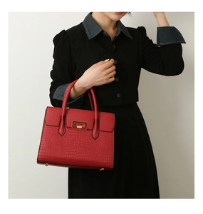 Detail of red embossed faux crocodile tote bag with elegant gold metal clasp on model
