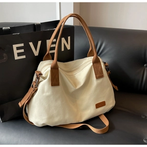 Close-up of cream canvas tote bag with brown straps and leather logo on a black sofa