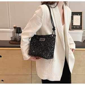 Détail du sac à main noir à paillettes avec plaque Fashion argentée sur costume blanc